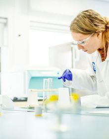 science student in lab coat stirring liquid in a beaker