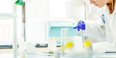 science student in lab coat stirring liquid in a beaker