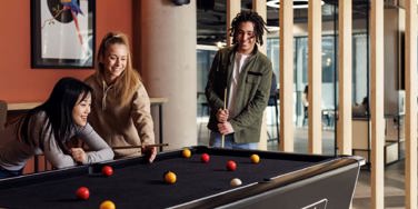 three people stood round a pool table