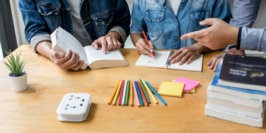 three people round a desk with books, notepads, pens and sticky notes