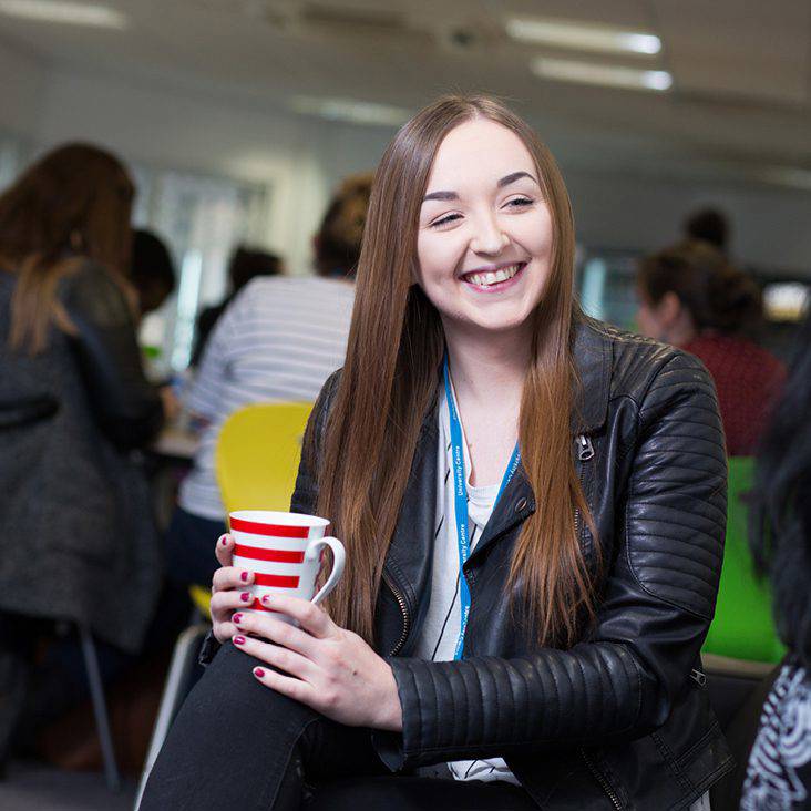 student sat smiling holding a red and white striped mug