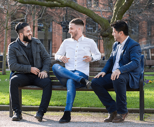 three people sit chatting on a park bench