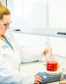 University Centre Leeds student in a lab coat measuring a red liquid in a measuring beaker