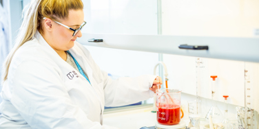 University Centre Leeds student in a lab coat measuring a red liquid in a measuring beaker