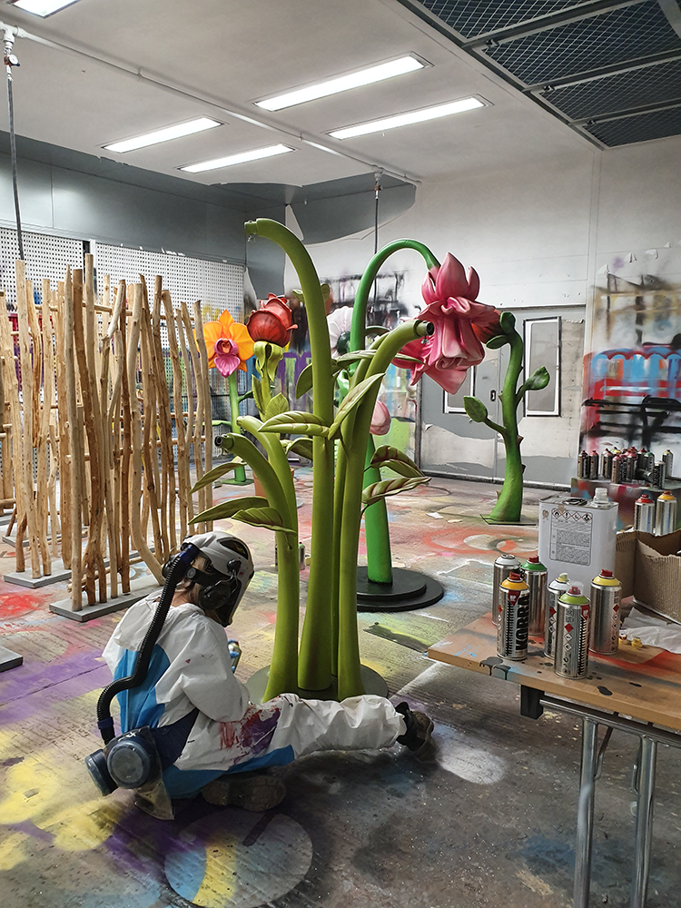 student in white paper overalls painting a big prop flower