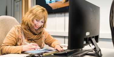 student writes on a tablet while sat at a desk with a monitor in front