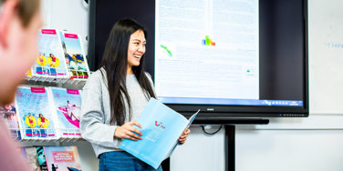 student stands at the front of a class with a TIU brochure