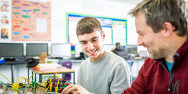 student and teacher stood over some electronics