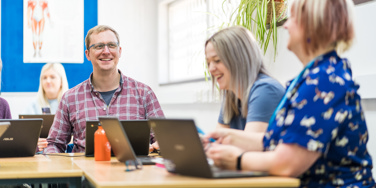 Group of people sat at desks with Chromebooks in front of them