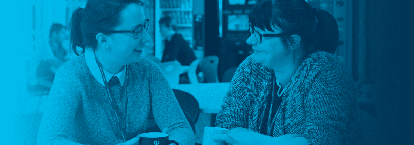 two staff members in a cafeteria holding cups of tea smiling with blue gradient over top